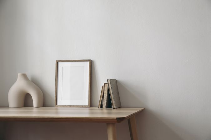 Blank poster on wooden table with empty vase and books