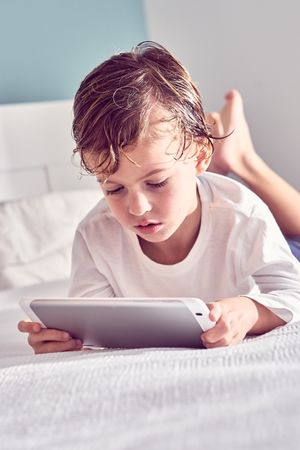 Boy lying on bed and watching video on tablet