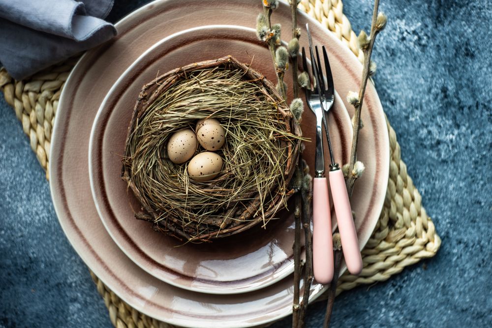 Top view of decorative eggs in delicate nest on ceramic pink plate on placemat