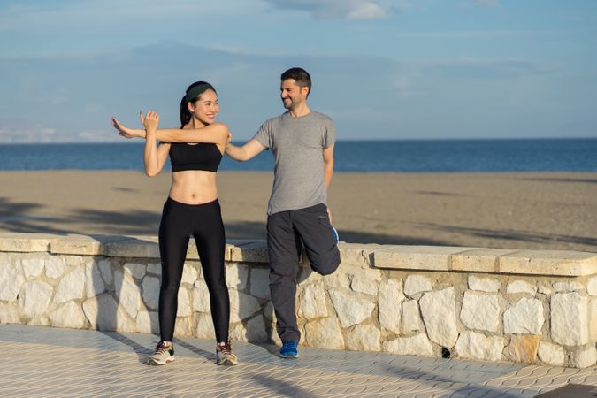 Young couple in active wear going stretching exercises together at seaside