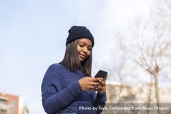 Female in wool hat and blue sweater checking smart phone on sunny day with space for text 4dlgL4
