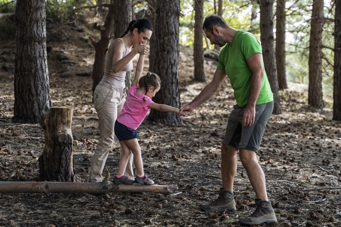 Parents helping daughter balance on log during forest walk adventure