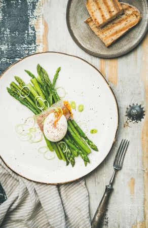 Asparagus and soft boiled egg on plate, on wooden table, with linen, and toast, and fork