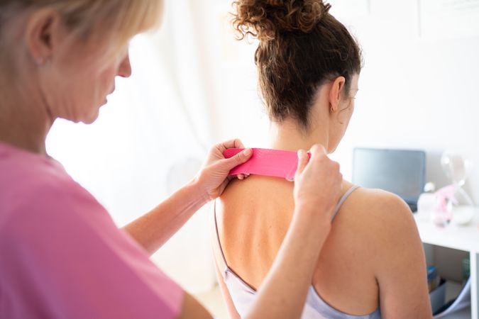 Osteopath using pink kinesiology tape on back of female patient