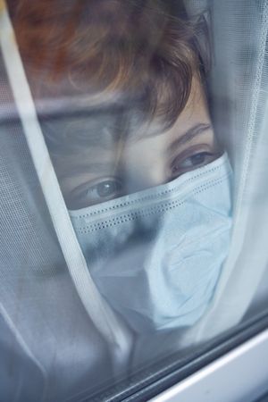 Crop boy in medical mask near window at home