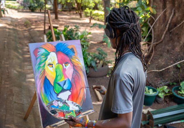 Black artist painting in a park while listening to music