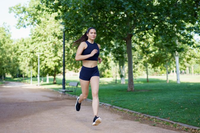 A young woman is jogging in a park, engaging in outdoor fitness and cardio to maintain her health and wellness
