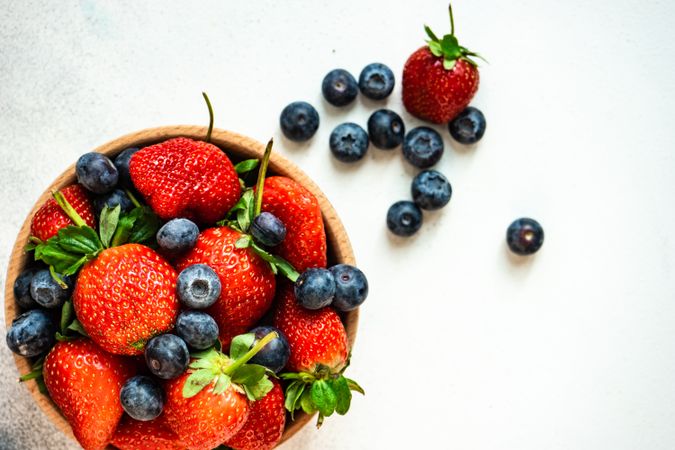 Top view of summer berries in wooden bowl full on stone background with copy space