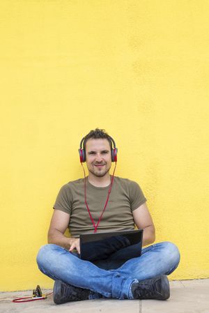 Content male with red headphones sitting outside looking at laptop