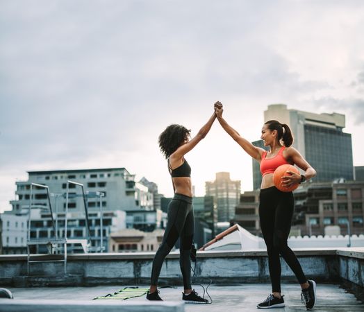Two women in fitness wear giving high five standing on rooftop during workout
