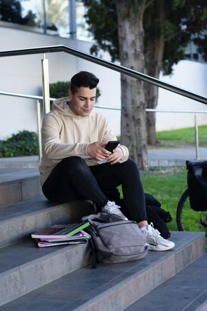 Young man sitting on a campus steps while using a mobile