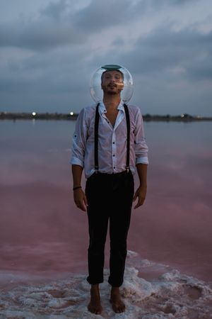 Man with fish tank on head standing at seashore