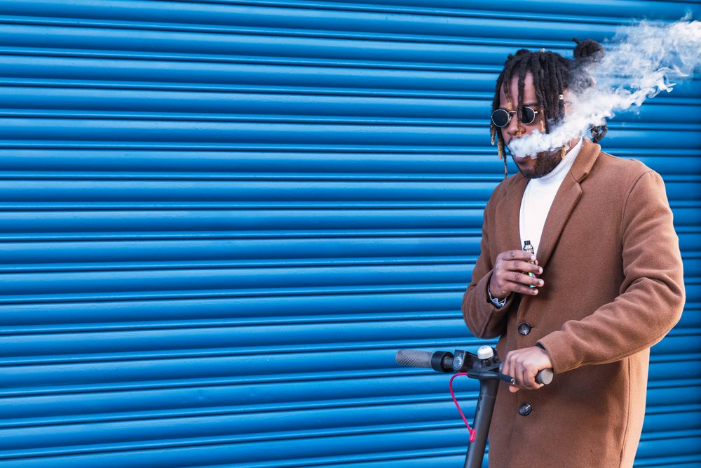 Hipster Black man with electronic cigarette on electric scooter
