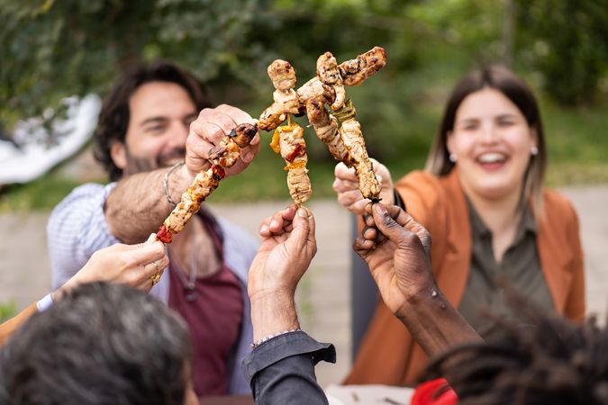 Friends raise skewers with skewers joking together while sitting at the picnic table