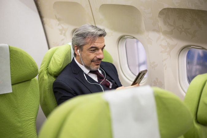 Man watching phone screen with ear buds in flight