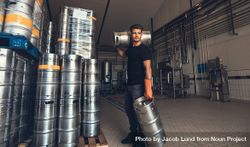 Young male brewer carrying kegs at brewery factory bEzEN0