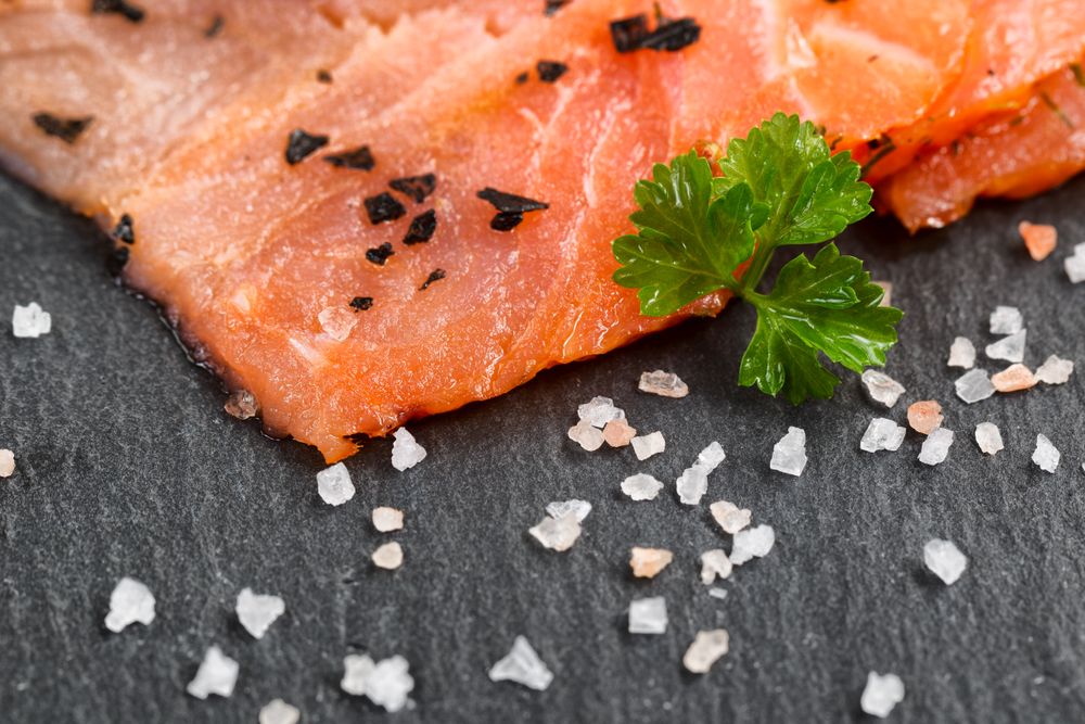 Smoked wild salmon slices with seasoning herbs on natural stone background