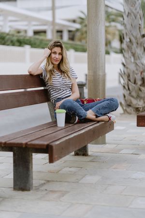 Confident woman with disposable cup of coffee sitting on street bench