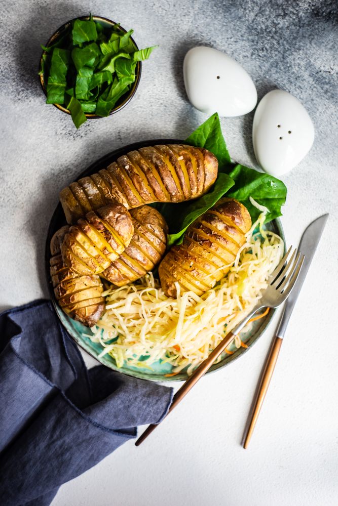 Top view of baked potato, spinach and cabbage salad on marble counter