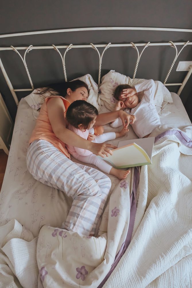 Looking down at mother reading story to her daughter and son lying in the bed