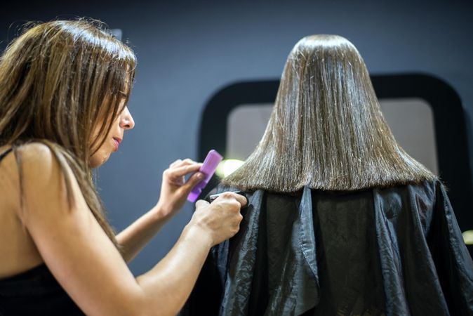 Hairdresser trimming ends of female client