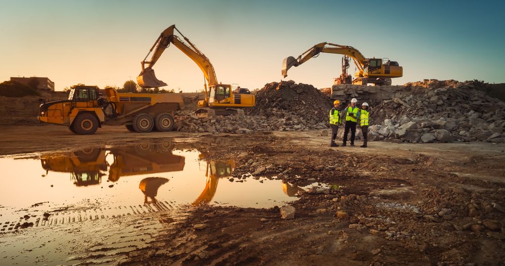 Aerial Drone Shot Of Construction Site With Heavy Machinery On Sunny Day: Diverse Team of Real Estate Developers Discussing Project. Engineer, Architect, Urban Planner Talking And Using Tablet.
