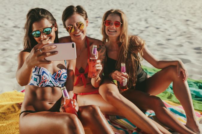 Happy women on vacation at a beach posing for a selfie wearing colorful sunglasses