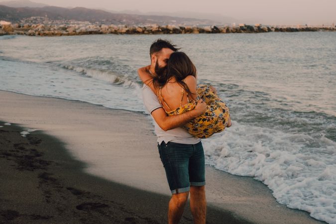 Amorous man carrying woman on arms along sandy beach