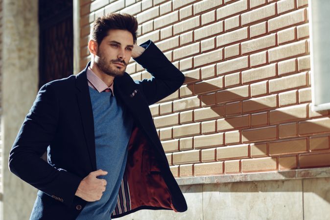 Man in smart suit leaning on brick wall with shadow of elbow