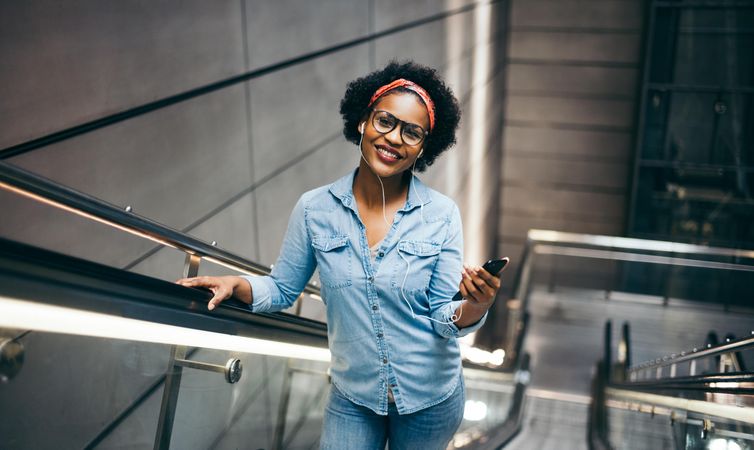 Woman smiling at camera while holding a phone on an escalator