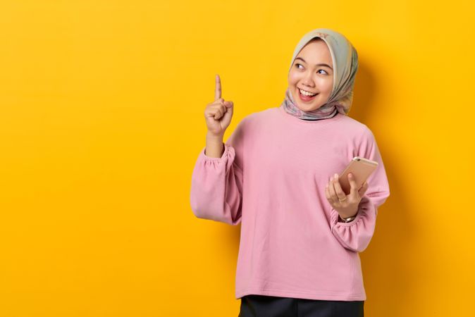 Excited Muslim woman on the phone and pointing upwards holding smart phone