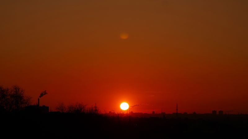 Panoramic orange sunset framing urban skyline with rising smoke