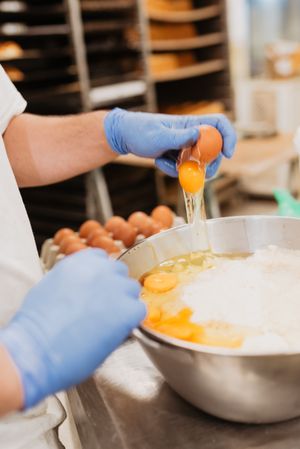 Crop baker breaking egg for pastry