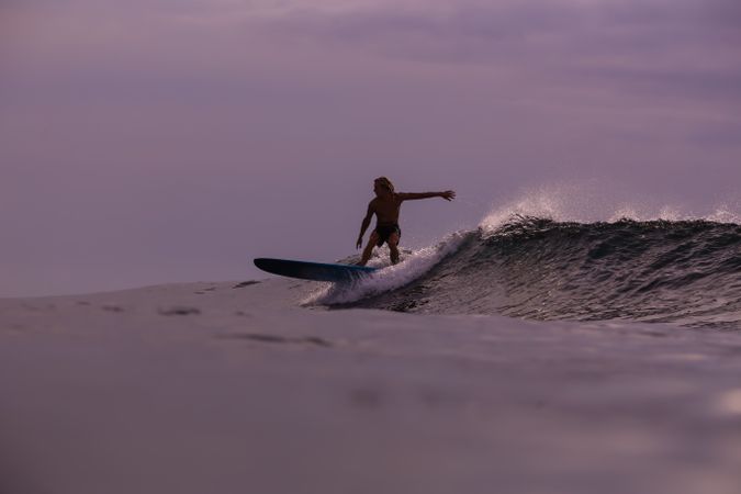 Man on surf board on waving water at sunset