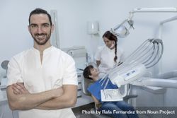 A portrait of a happy dentist with smiling teenage patient sitting in the background 0WYA64