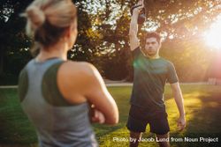 Healthy young man with female trainer exercising with kettlebell in the park bxdBvb