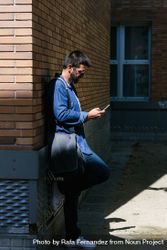 Man leaning on brick wall outside checking phone 5or2k0