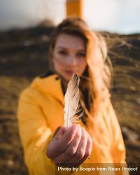 Young woman in yellow jacket holding light feather 41OLO0
