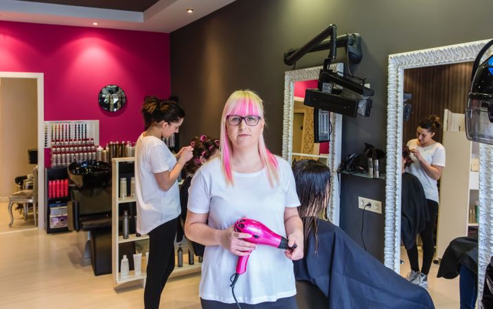 Woman with pink hair holding pink hairdryer in salon