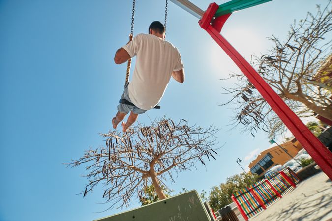 Man swinging on playground in sunlight