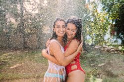 Friends in swimsuits hugging under water drops