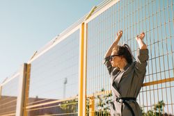 Stylish woman in sunglasses raising hands and leaning on lattice