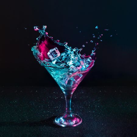 Martini cocktail drink splash with ice cubes in neon iridescent pink and blue colors