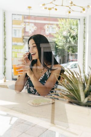 Woman with healthy drink talking phone in cafe