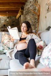 Relaxed pregnant woman enjoying reading a book on her home sofa 56YxV0
