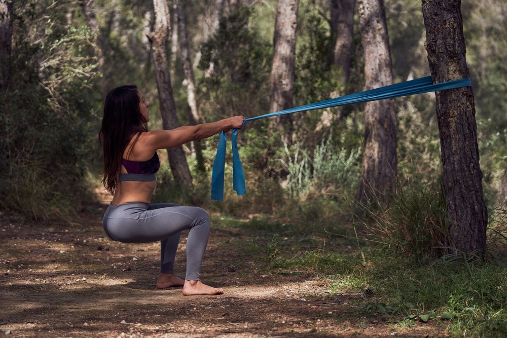 Fit female doing squats with elastic band around tree