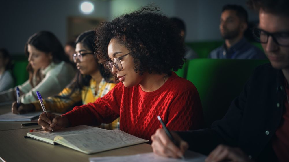Black Young Woman Writing Down a Summary from the Lecture in Her Notebook