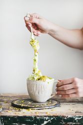 Hand taking large spoonful of up of pistachio ice cream with spoon on white background