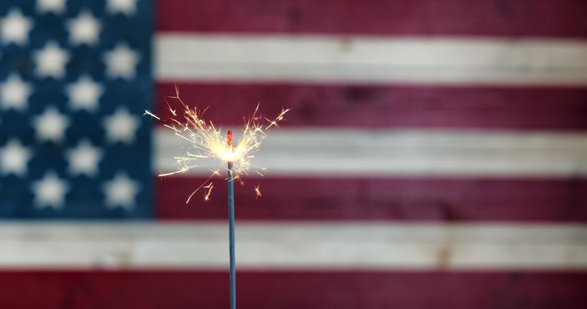 Glowing sparkler with rustic wooden flag of USA