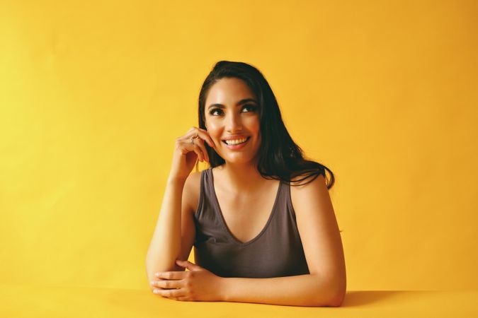 Hispanic woman looking up smiling while sitting in yellow room, copy space